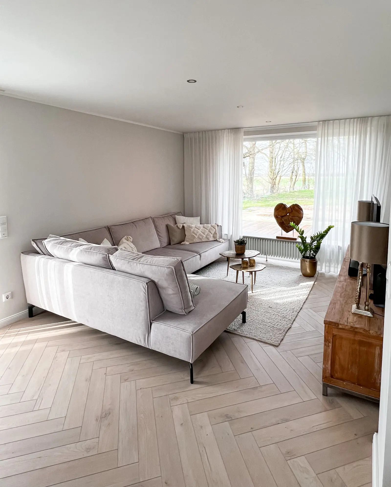 Wohnzimmer mit hellem Cortec-Vinylboden in Fischgrät-Parkettoptik und bodentiefen Fenstern
